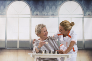 Senior playing chess accompanied by a nurse